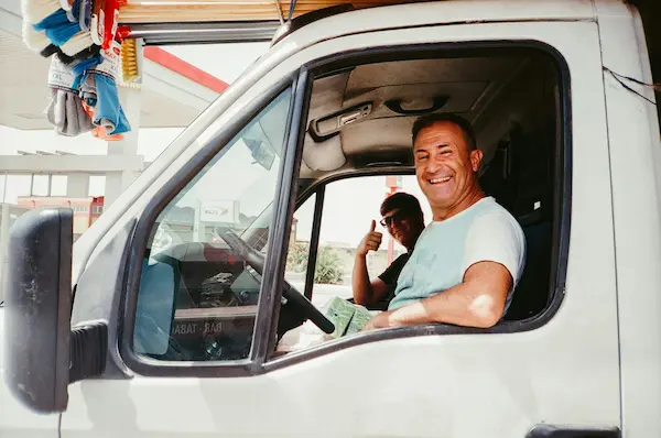 Two men smiling inside a white service vehicle, one giving a thumbs up from the passenger seat.