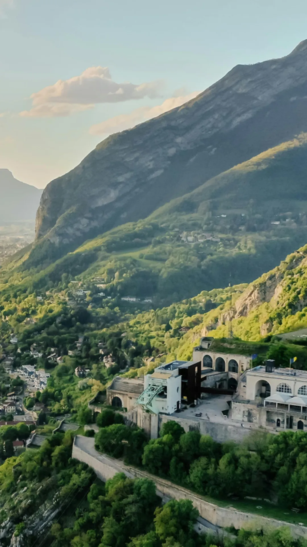 Vue aérienne d'une forteresse au sommet d'une colline avec montagnes verdoyantes au fond.