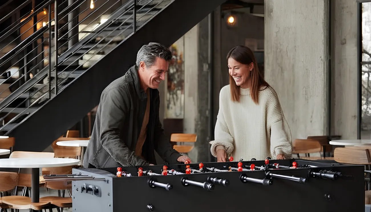 A smiling man and woman are playing table football in a modern industrial café.