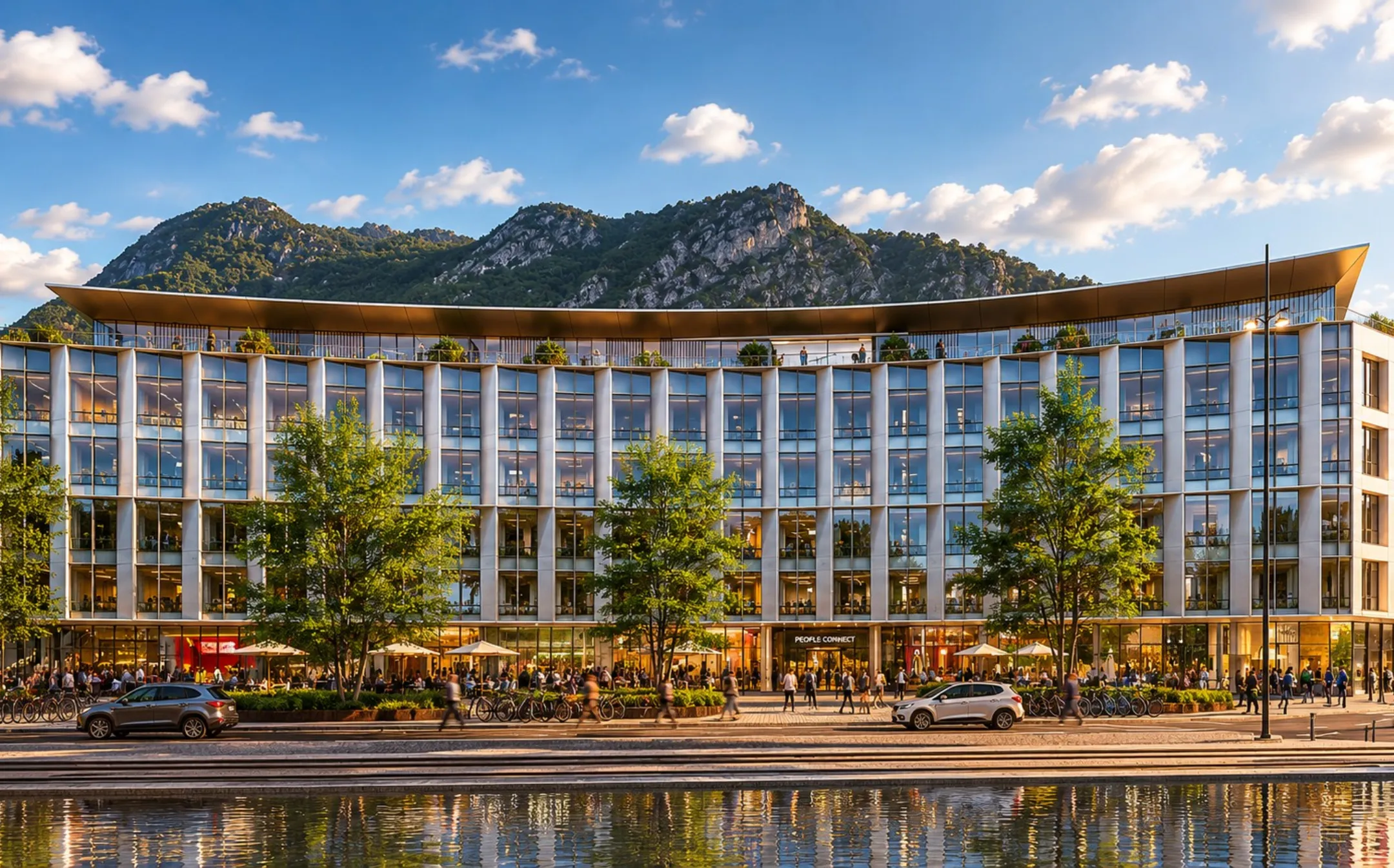 Glass facade of a large modern building with trees, pedestrians and mountains in the background.