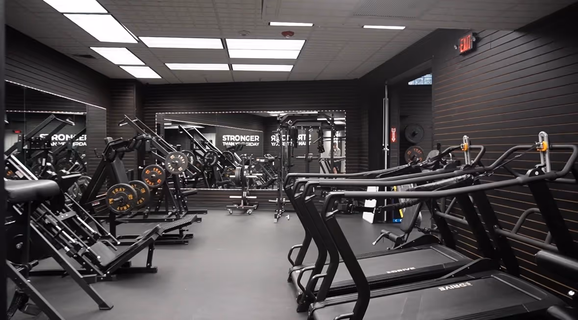 Modern gym interior with treadmills, weightlifting machines, and large mirrors on dark walls.