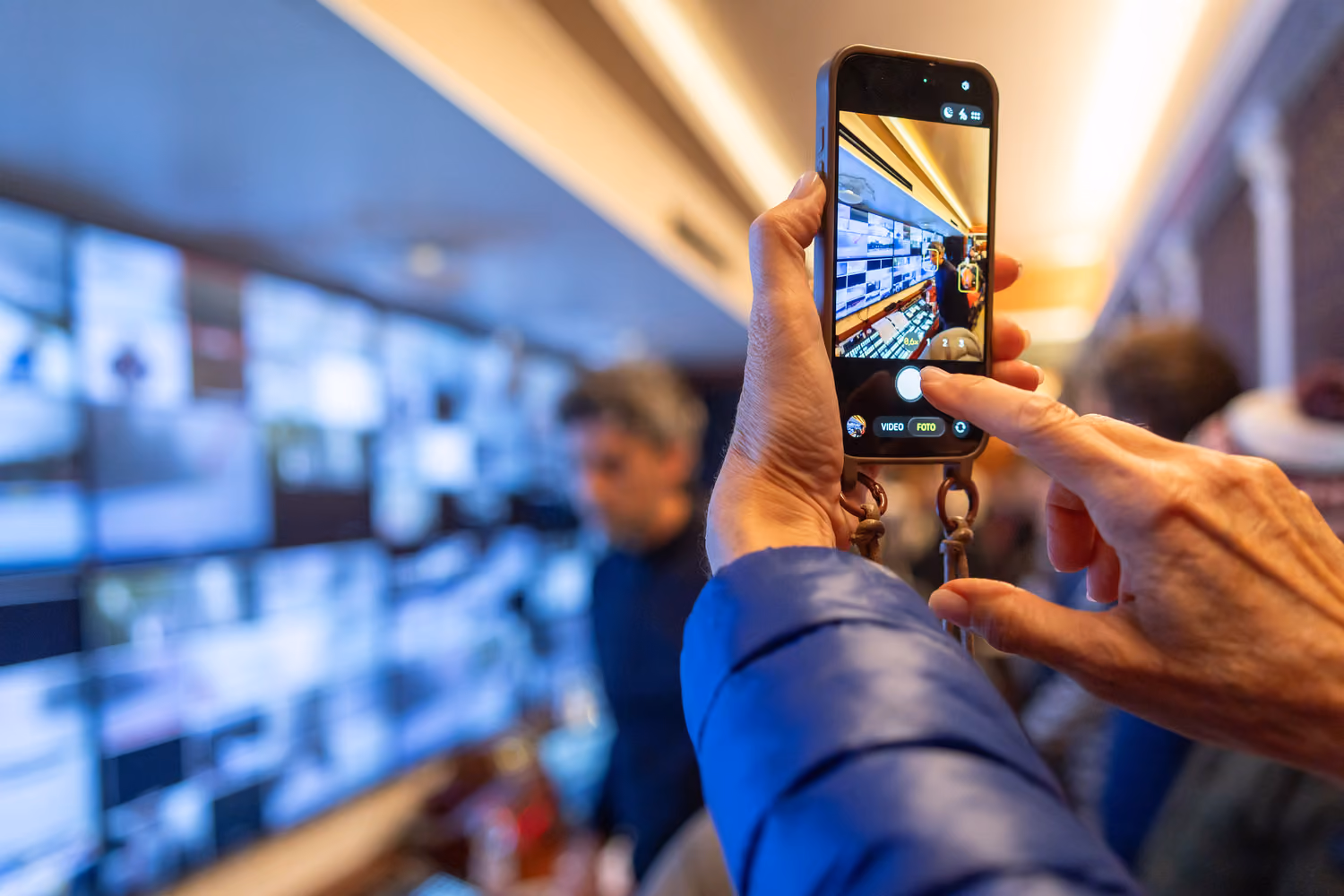 Person photographing wall of glowing screens with smartphone