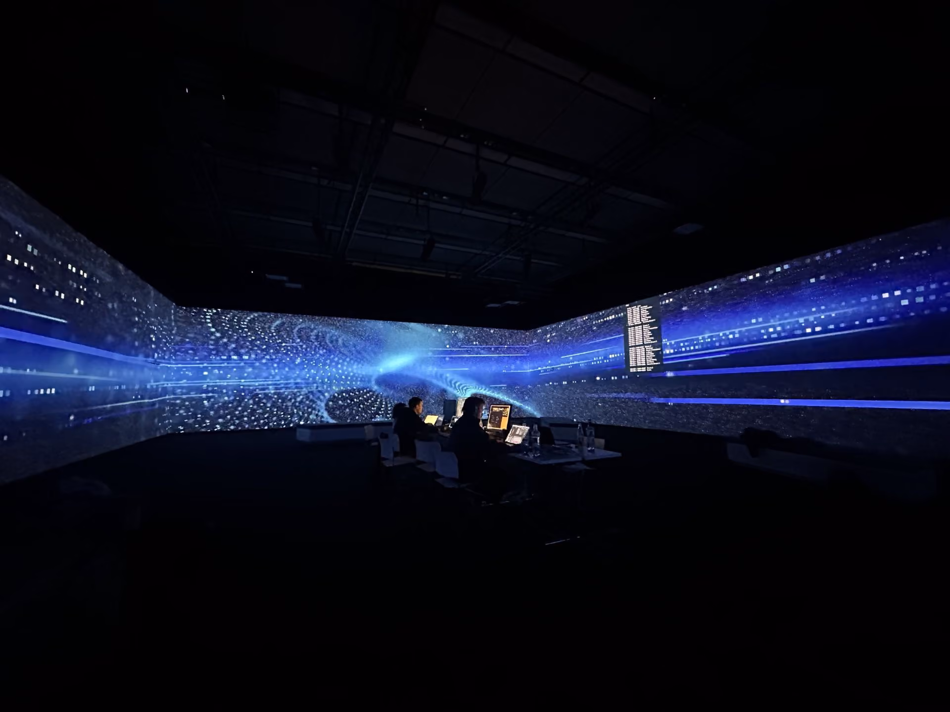 Blue data projections in dark room with people at laptops
