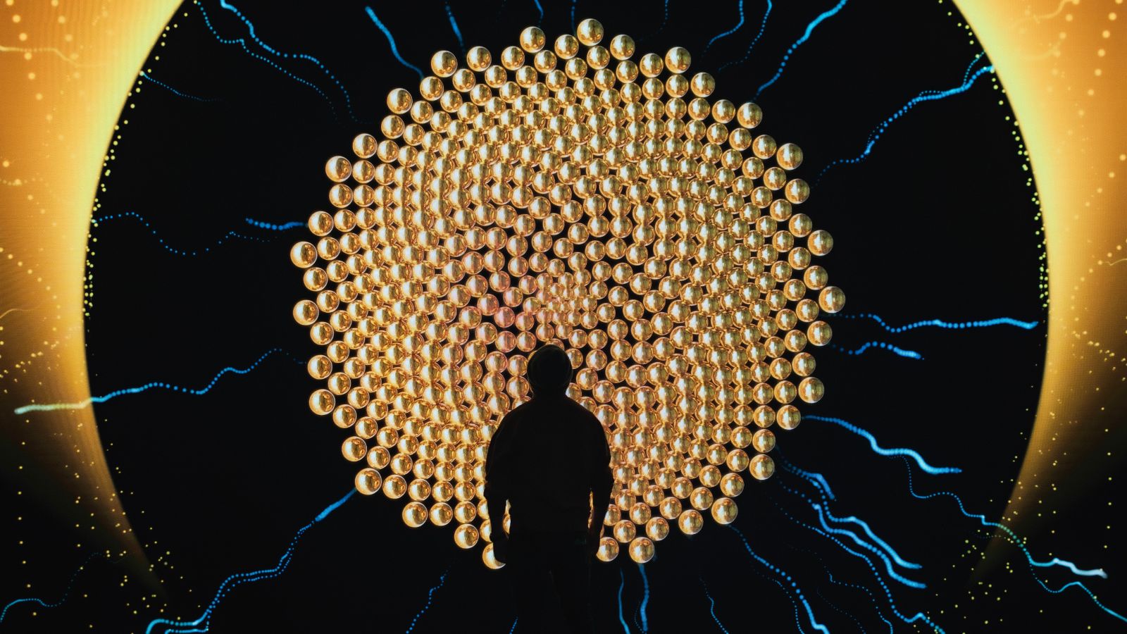Person faces a circular display of golden spheres and blue waves