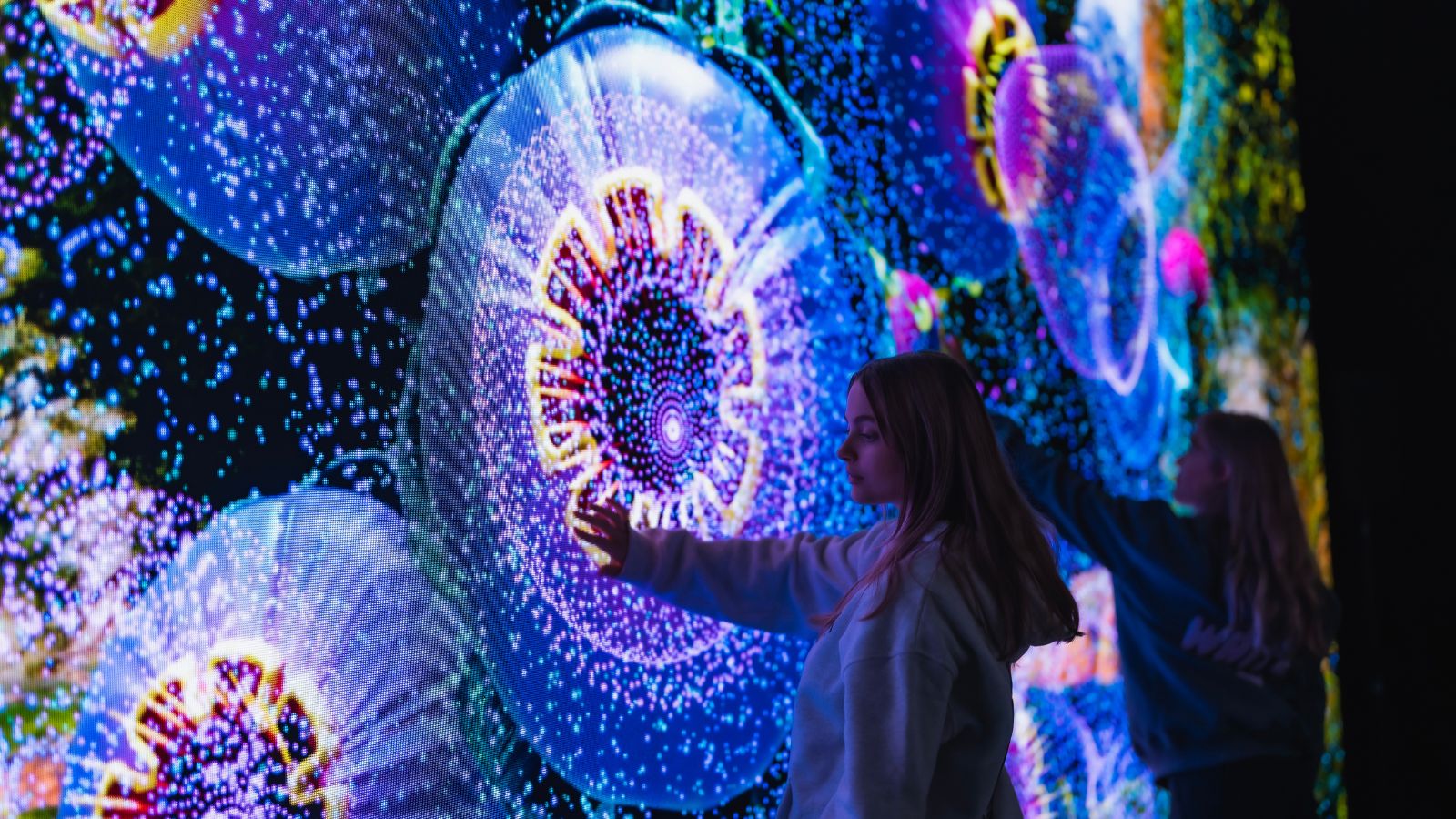 Girl reaches toward glowing blue and purple bioluminescent patterns