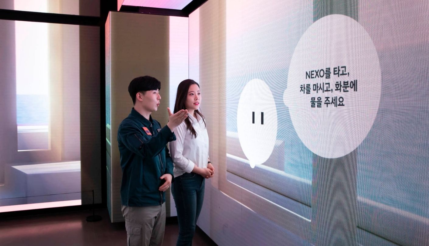 Staff gesture toward a large screen displaying Korean interactive text