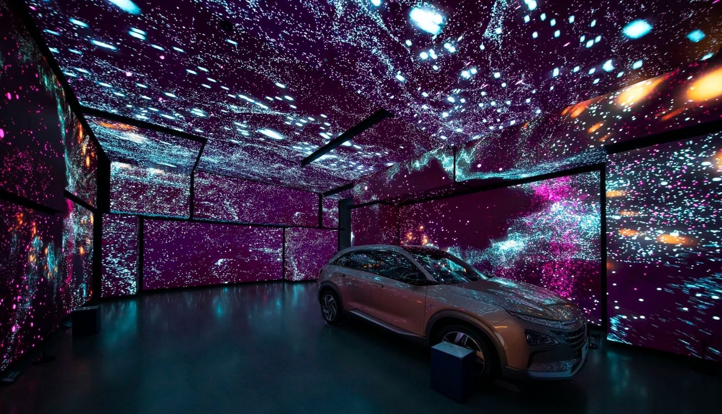 Purple and cyan light particles fill walls and ceiling above a car