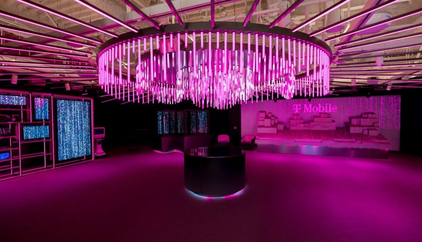 Pink-lit briefing room with circular tube chandelier and digital screens