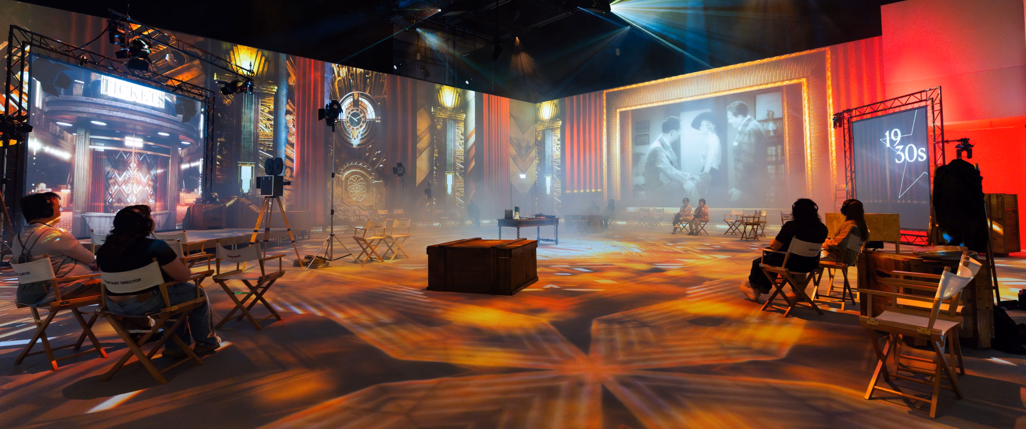 Visitors in director chairs watch 1930s visuals on wraparound screens