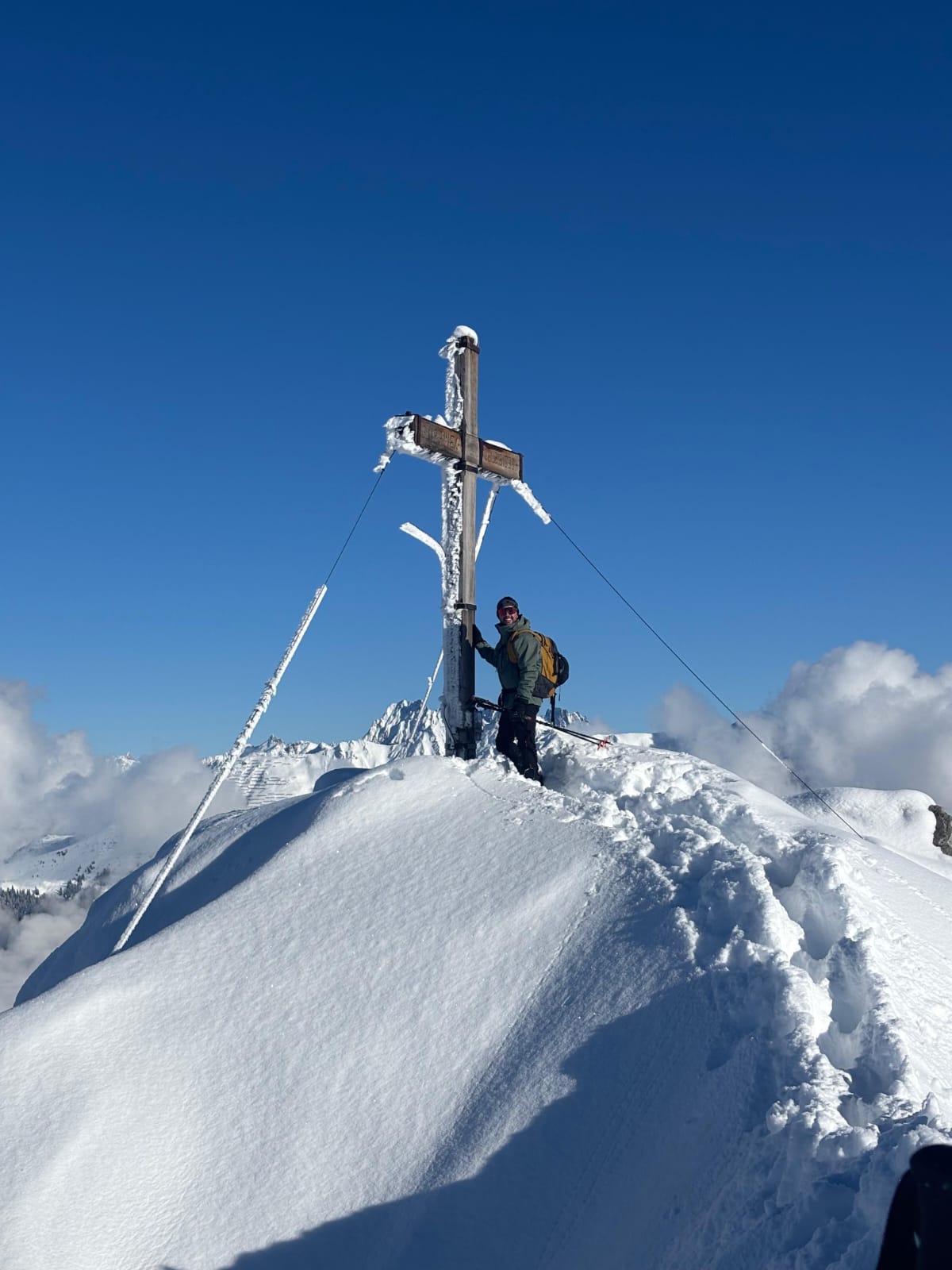 the author on a sunny and snowy summit, next to a wooden summit cross