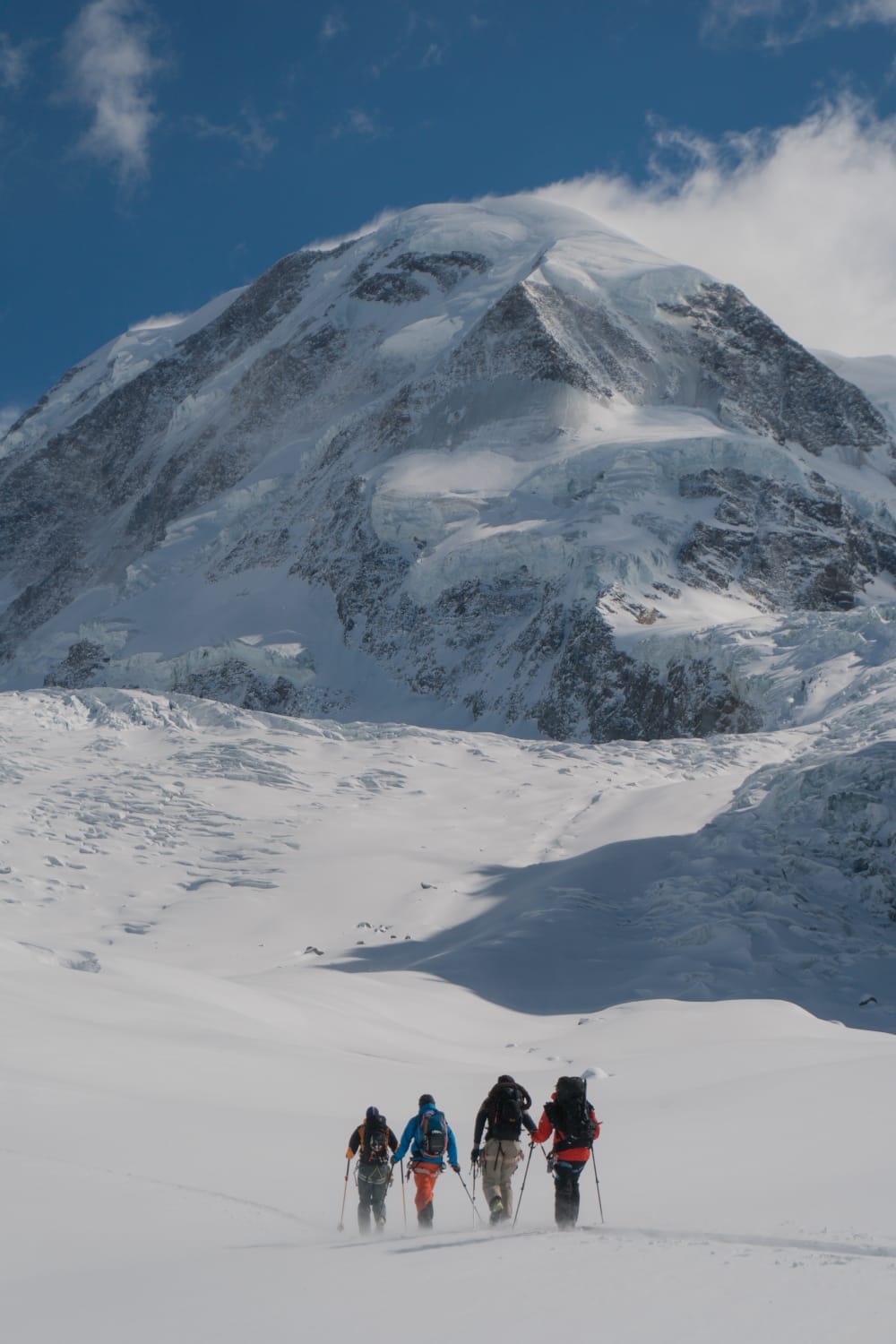 A group of mountaineers on a plateau, snow drifts in the wind, in the background is a stormy mountain peak