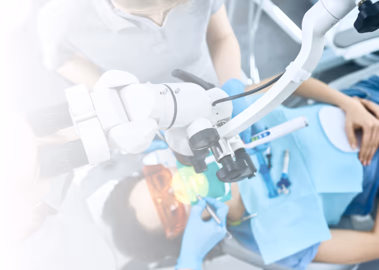 Dentist wearing gloves using a dental microscope to treat a patient reclining in the dental chair.
