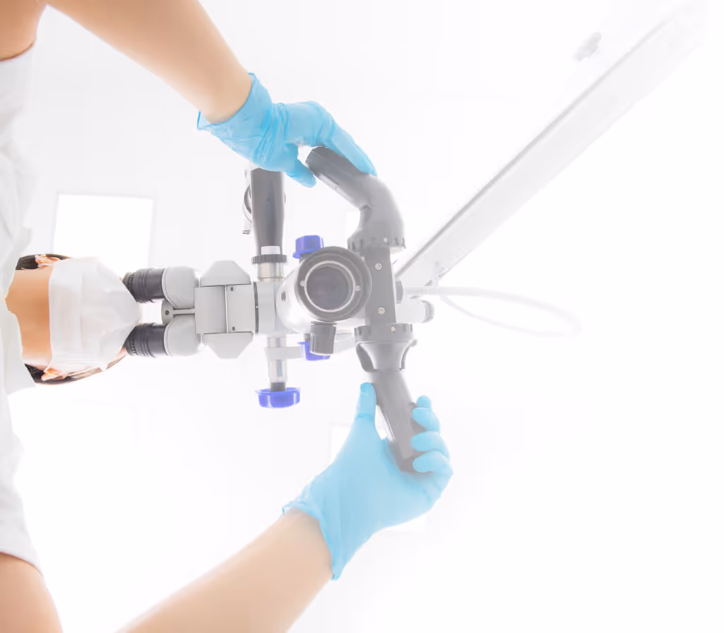 Medical professional wearing blue gloves and mask adjusting a surgical microscope.
