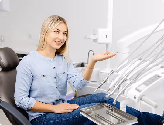 Smiling woman sitting in dentist chair gesturing toward dental equipment.