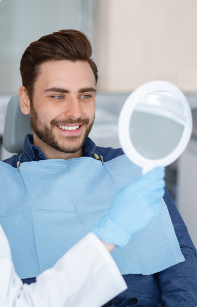 Smiling man in dental chair looking at his reflection in a handheld mirror.