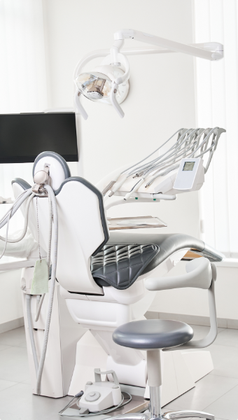 Empty modern dental chair with attached tools and overhead dental light in a bright clinic room.
