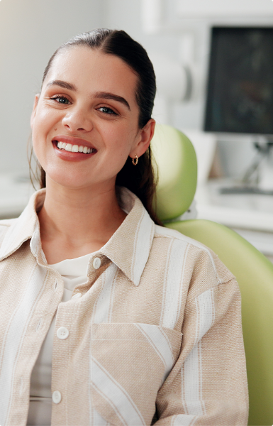 Smiling young woman with dark hair seated in a light green chair in a bright room.