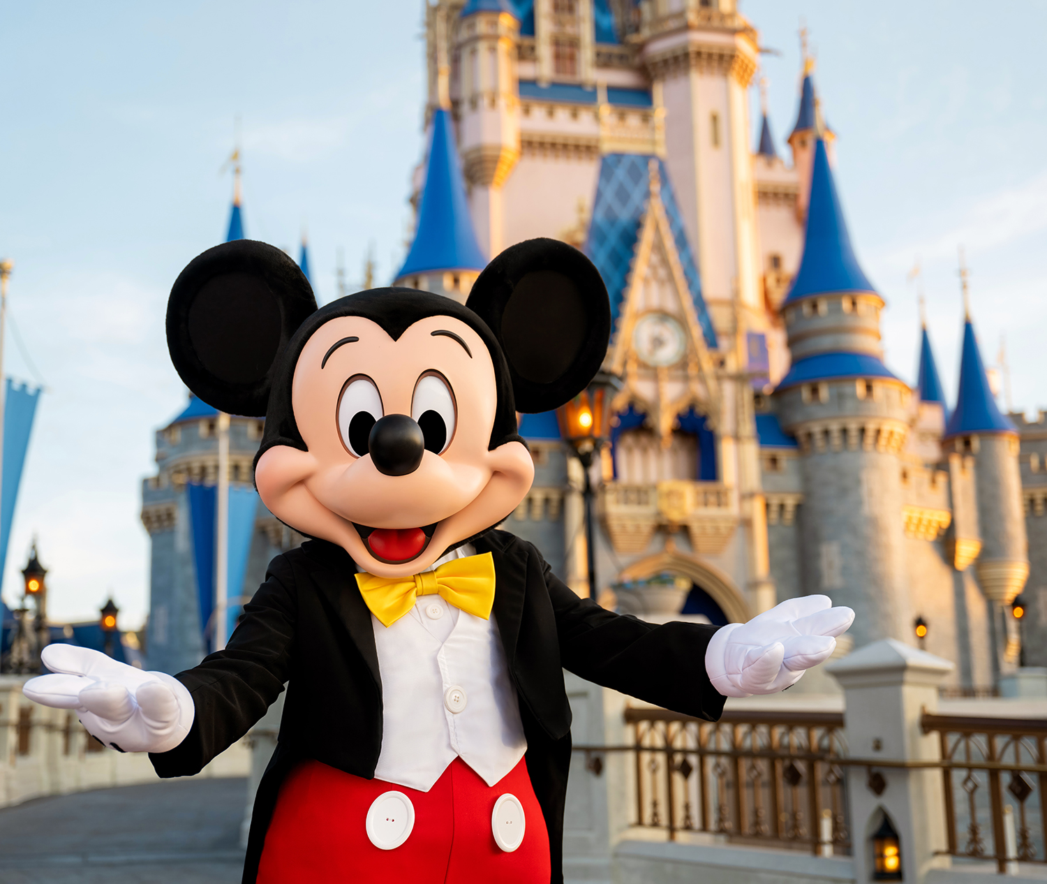 Mickey Mouse in a tuxedo with a yellow bow tie in front of Cinderella Castle at Disney World.