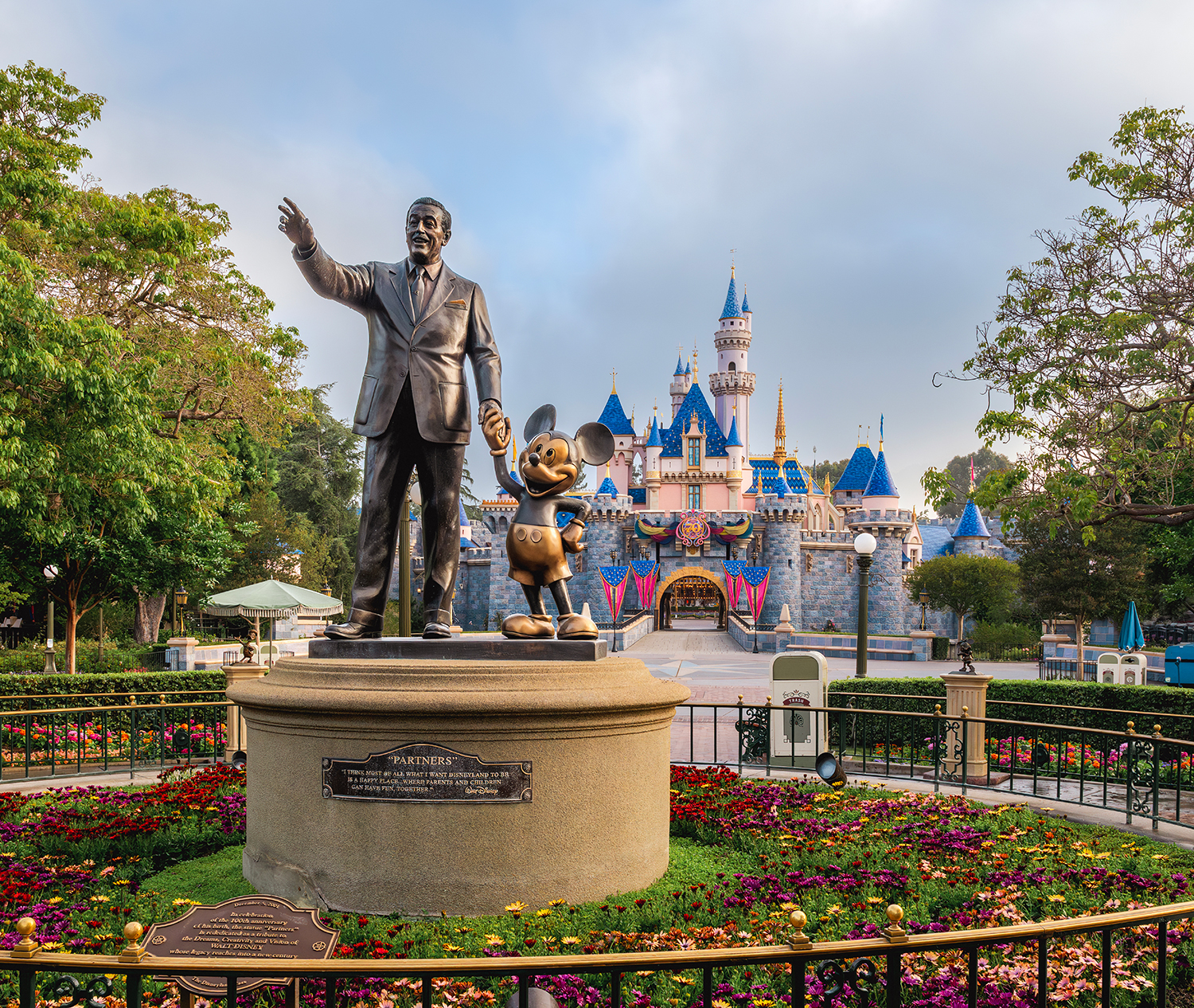 Statue of Walt Disney holding hands with Mickey Mouse in front of Disneyland's Sleeping Beauty Castle.