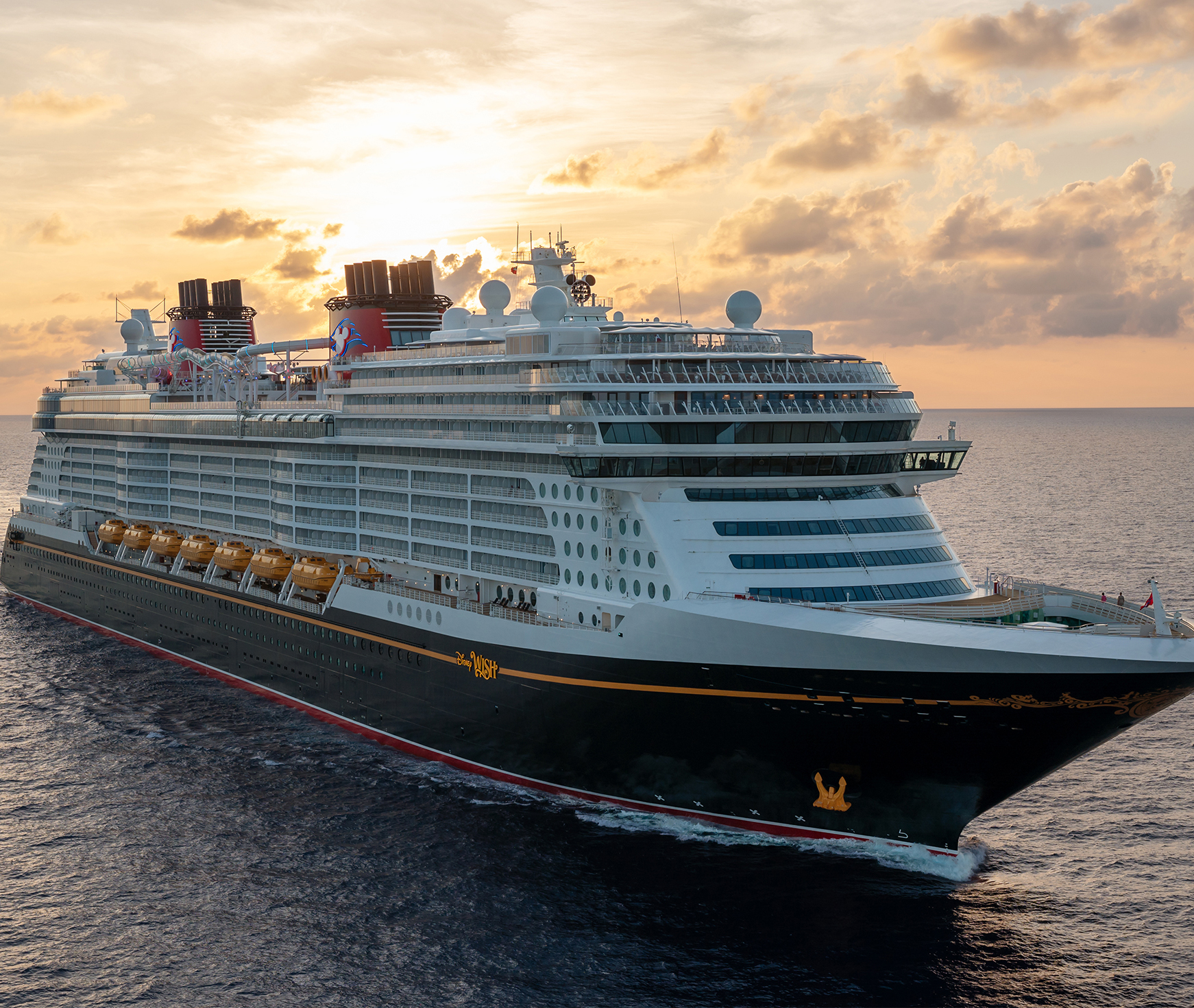Large Disney cruise ship sailing on the ocean during a golden sunset.