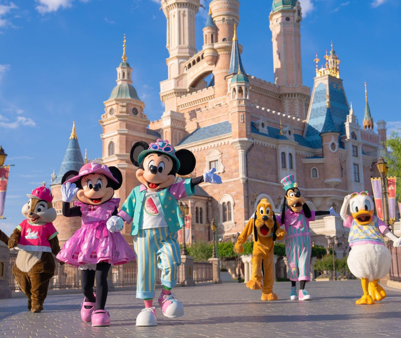 Disney characters Mickey, Minnie, Pluto, Goofy, Donald, and Chip in colorful clothes in front of a castle.