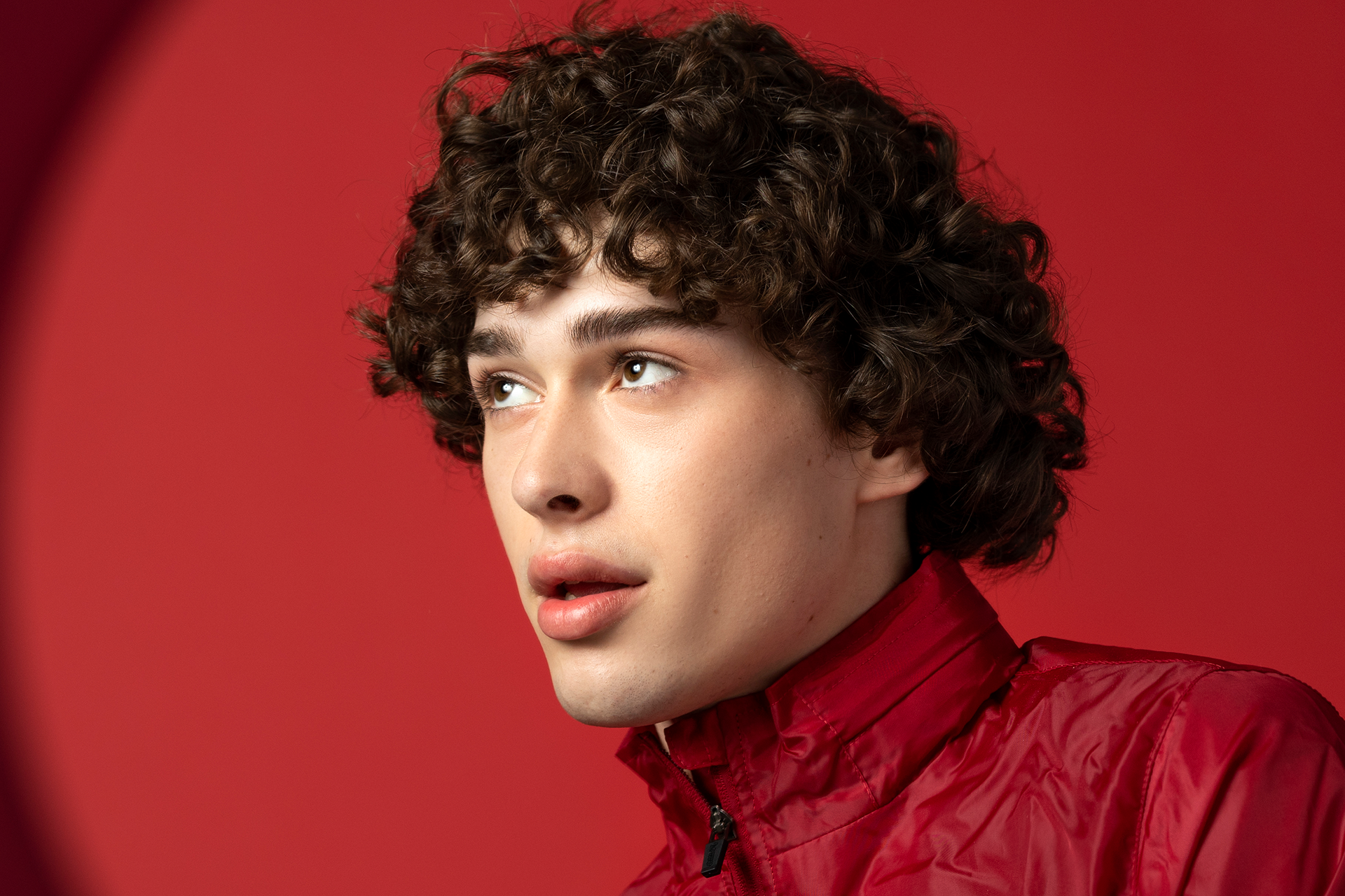 A man with curly hair wearing a red jacket.