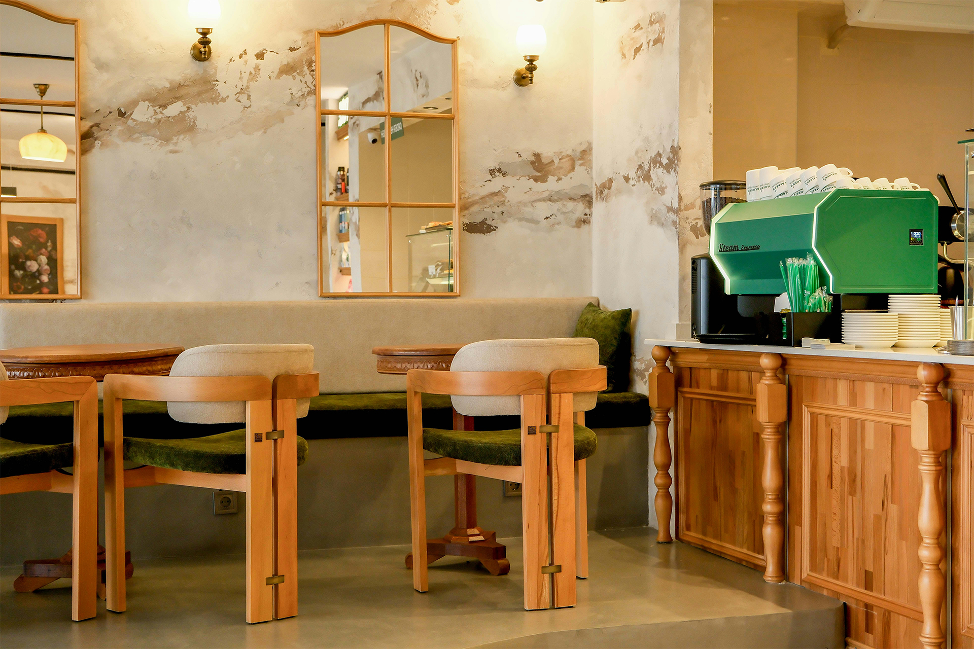 Cozy cafe interior with wooden chairs, tables, and a green espresso machine on a wooden counter.