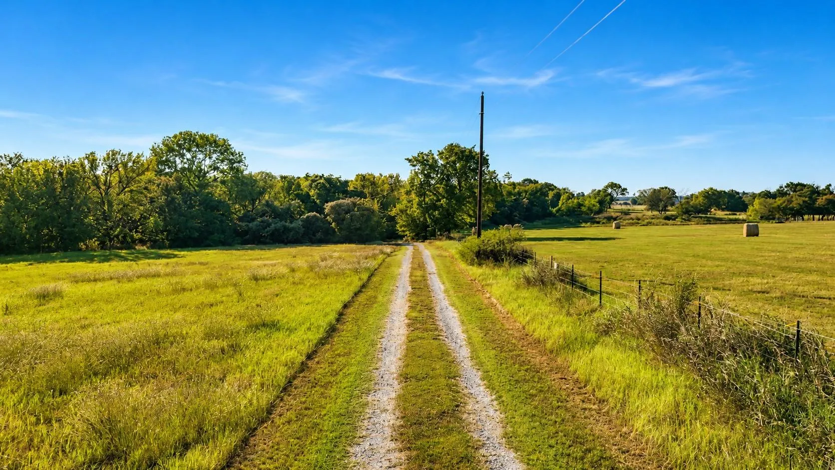 Gravel drive running between open pasture under a clear Texas sky