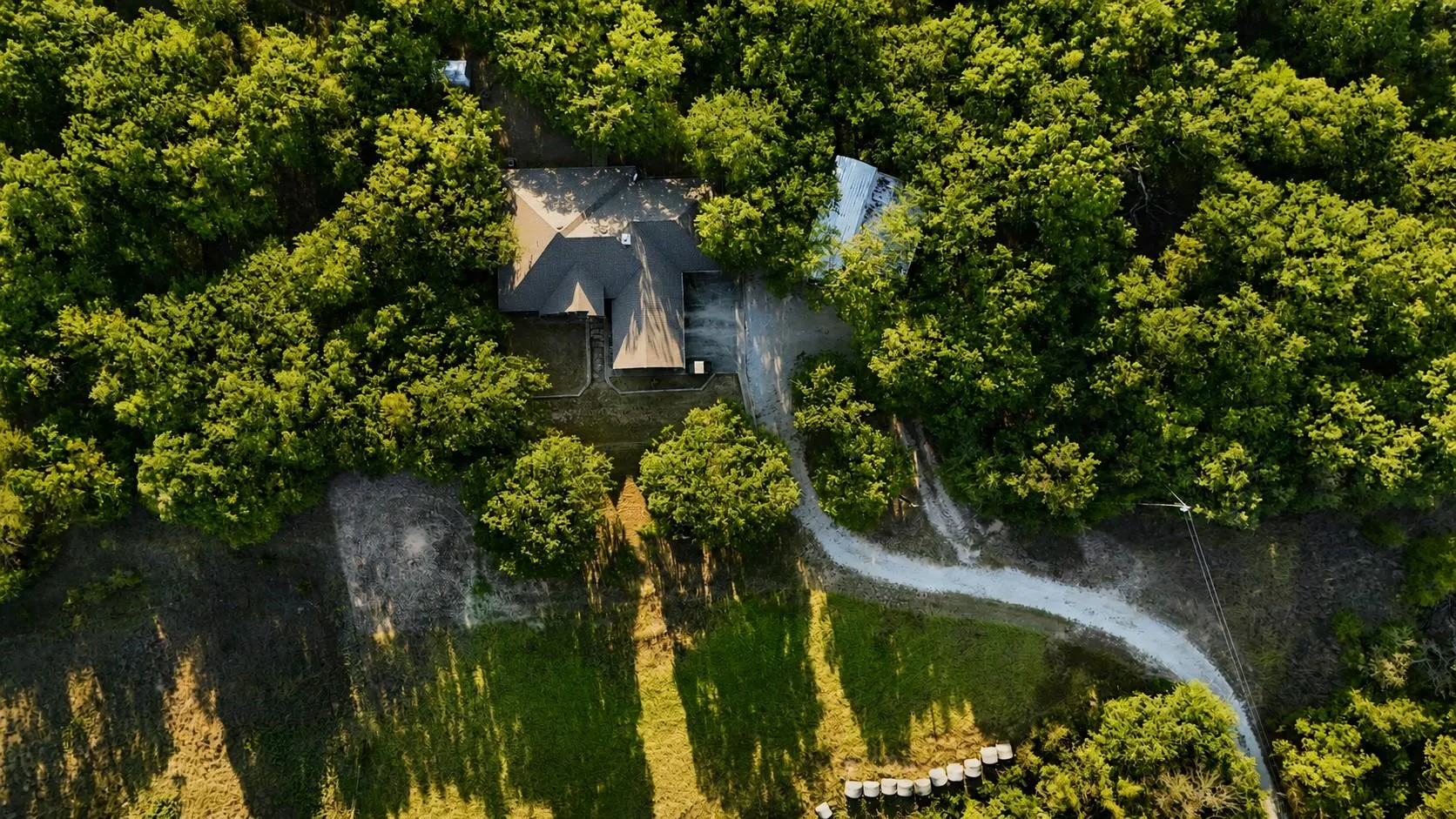 Aerial view of a rural home tucked into wooded acreage with a long gravel drive