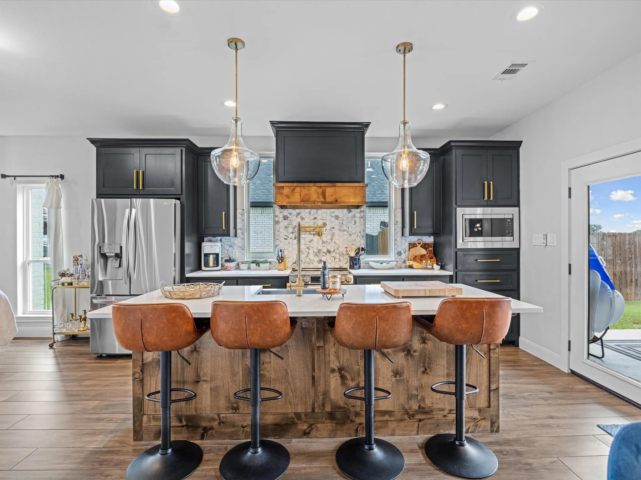 Farmhouse kitchen with dark cabinetry, brass fixtures and a wood island with leather bar stools