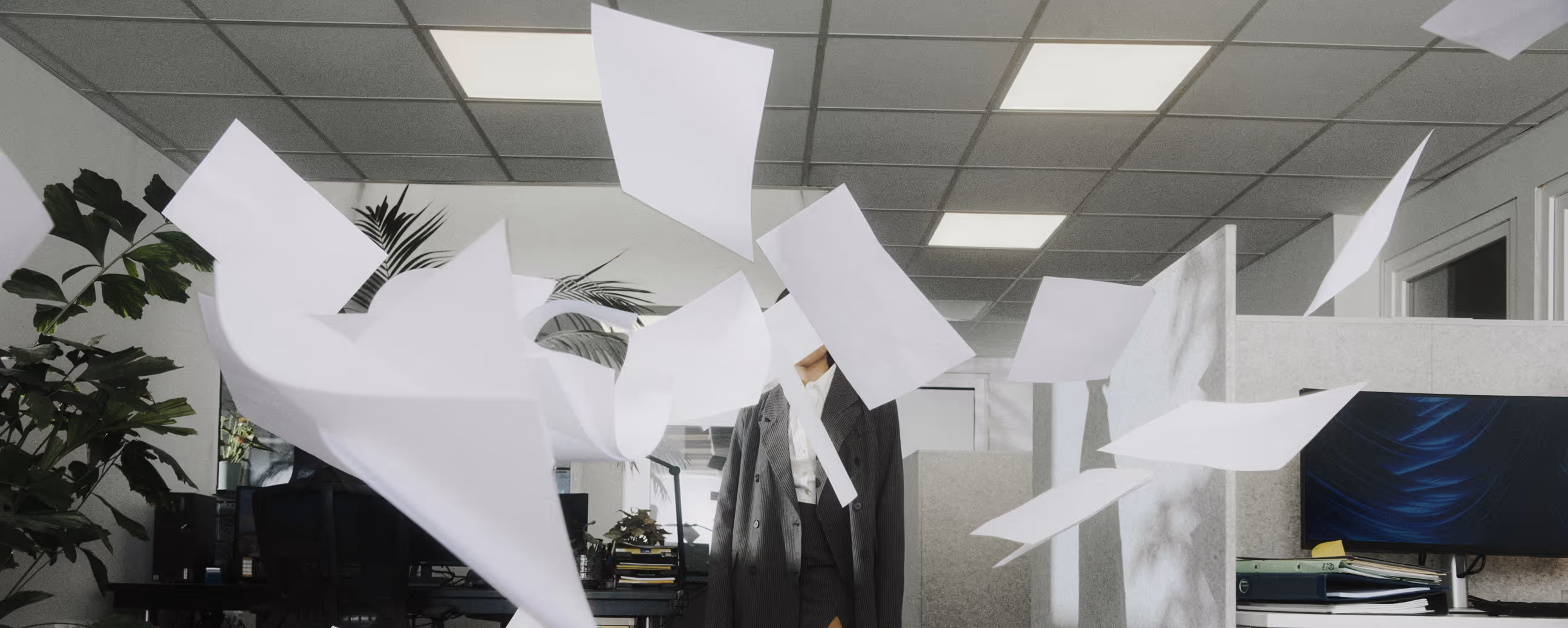 Personne en costume gris dans un bureau avec des feuilles de papier blanches volant autour.