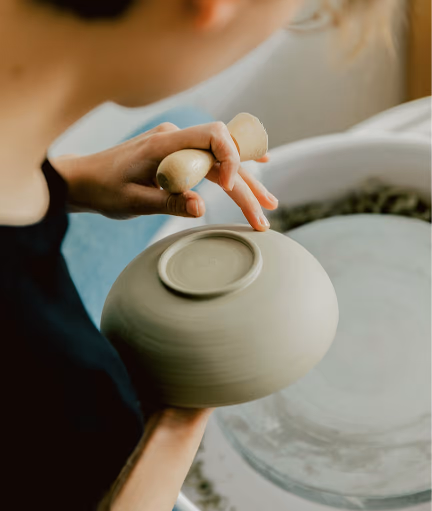 Une personne façonne un bol en argile en utilisant un outil en bois pour lisser le dessous.