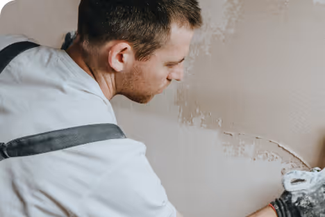 Un homme repeignant un mur avec un rouleau, portant une salopette blanche et un t-shirt bleu.