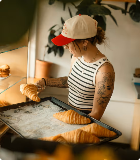 Femme avec casquette sert un croissant d'un plateau dans une boulangerie moderne.