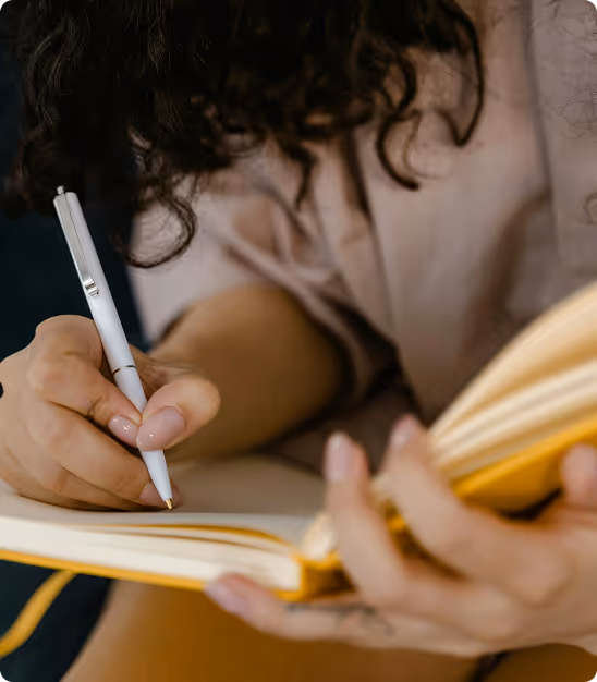 Personne tenant un stylo blanc et écrivant dans un carnet jaune tout en tenant des pages.