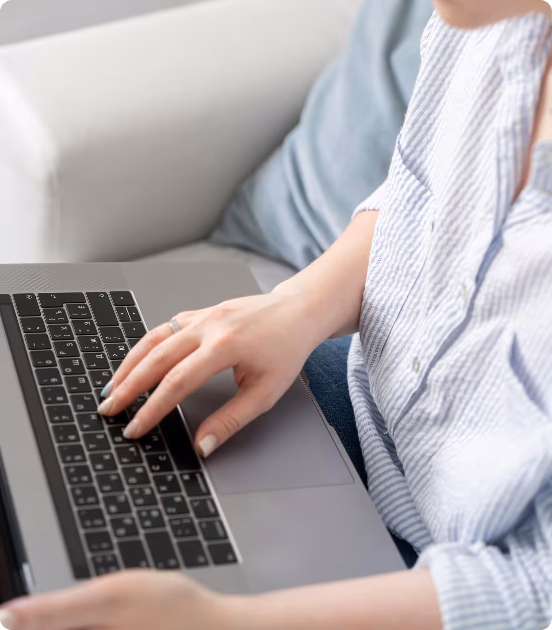 Person wearing striped shirt typing on a laptop keyboard while sitting on a couch.