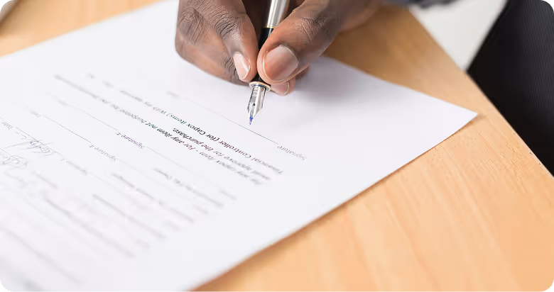 Une main tenant un stylo plume signant un document officiel sur une table en bois.