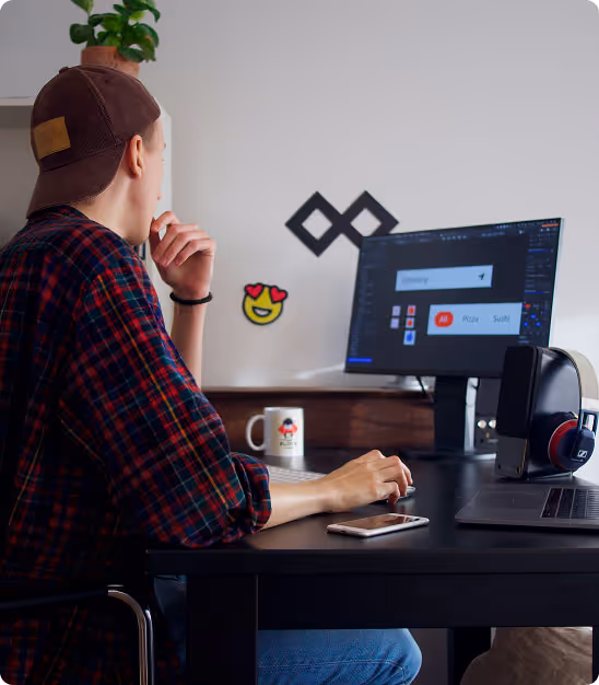 Jeune homme portant une casquette à l'envers travaille sur un ordinateur à son bureau.