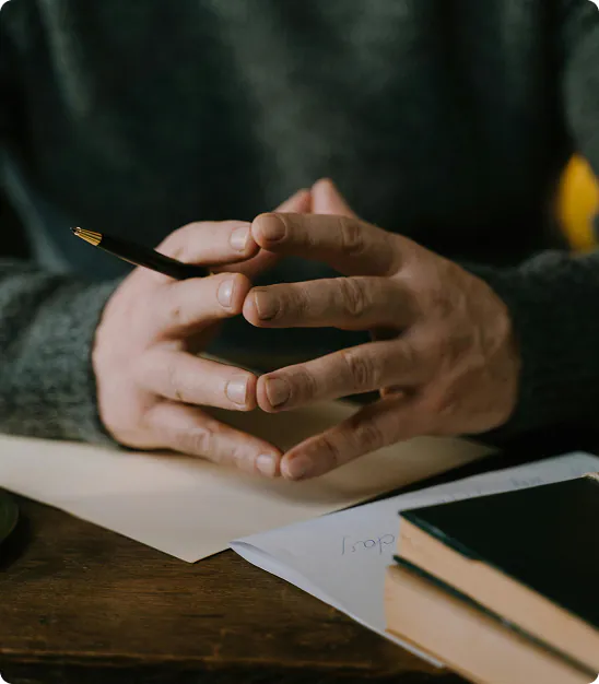 Mains tenant un stylo au-dessus de papiers avec deux livres sur une table en bois.