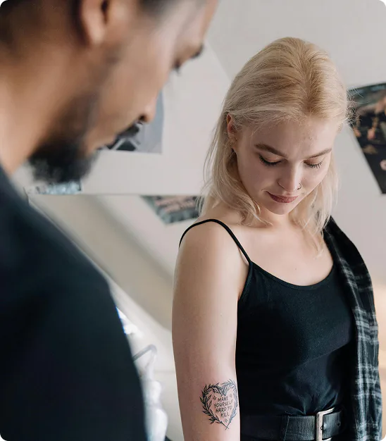 Jeune femme blonde montrant son tatouage sur le bras disant "Make yourself hard to kill".