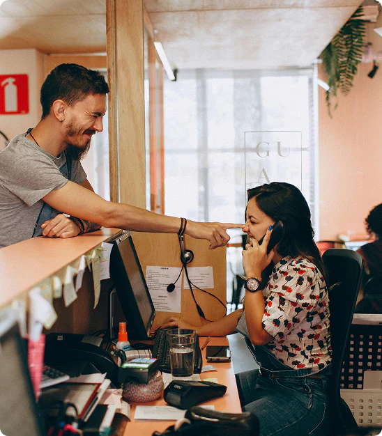 Un homme souriant touche le nez d'une femme parlant au téléphone à un bureau.