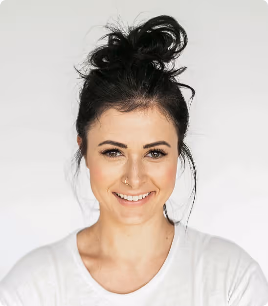 Femme souriante aux cheveux noirs attachés en chignon avec un anneau au nez, portant un t-shirt blanc.