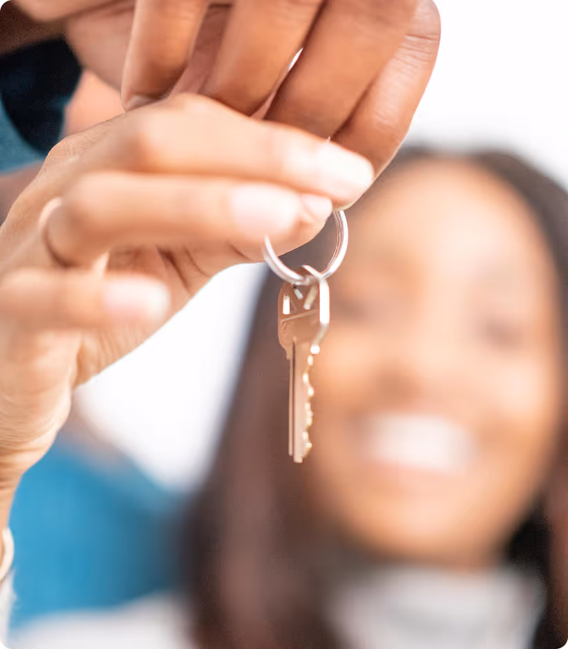 Une main tenant un trousseau de clés avec une femme souriante floue en arrière-plan.