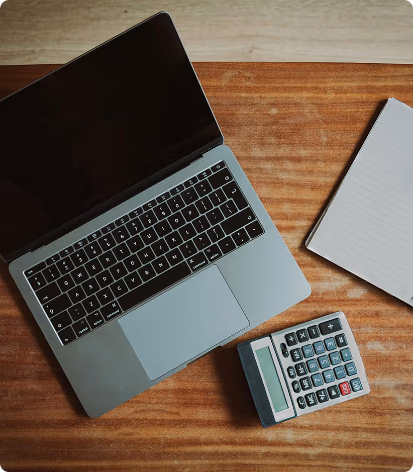 Ordinateur portable ouvert, calculatrice et carnet à lignes sur une surface en bois.