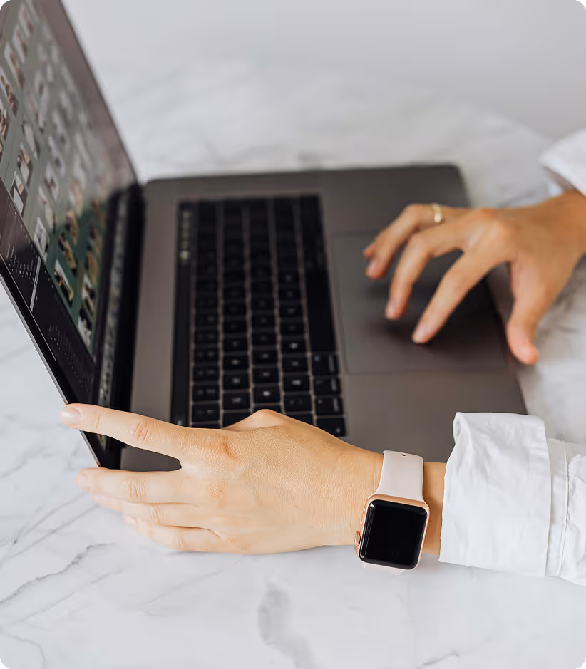 Personne utilisant un ordinateur portable sur une table, portant une montre connectée rose.
