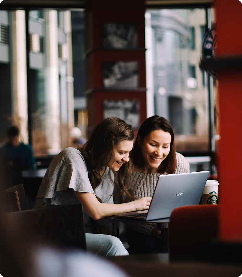 Deux femmes souriantes regardant un ordinateur portable dans un café avec une tasse Starbucks.