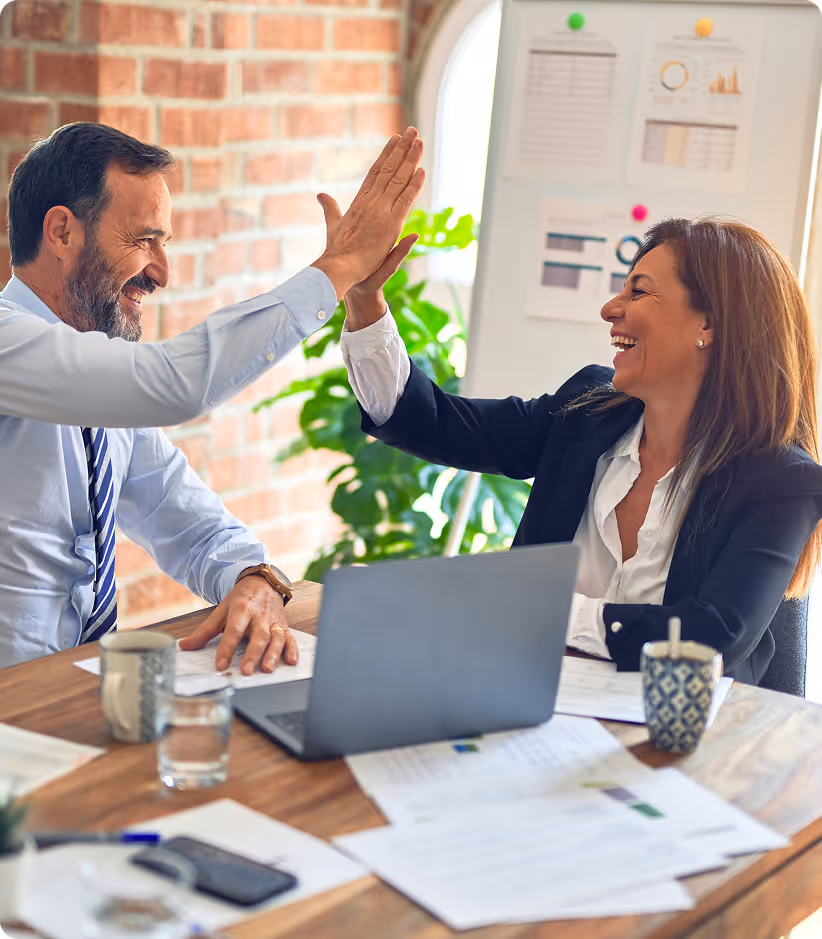 Deux collègues, un homme et une femme, se font un high-five joyeux lors d'une réunion au bureau.