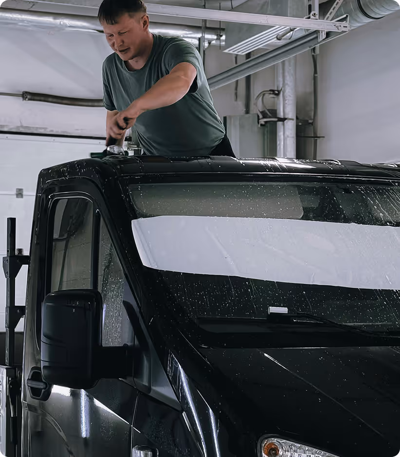 Un homme répare le toit d'un véhicule noir dans un garage industriel.