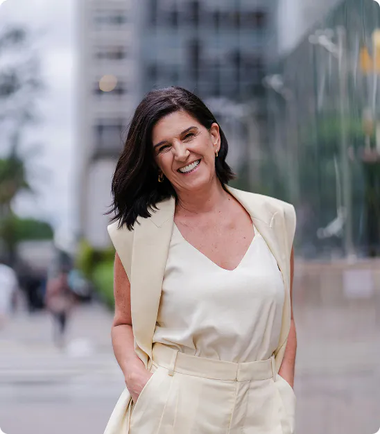 Femme souriante en tailleur crème avec les mains dans les poches en milieu urbain.