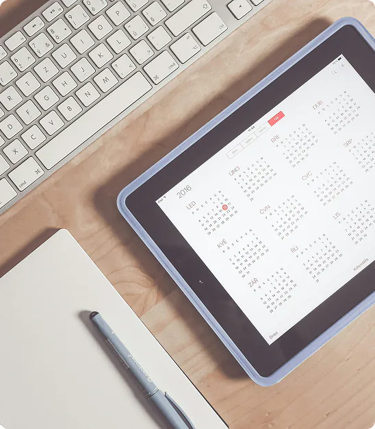 Clavier, tablette affichant un calendrier 2016 en français, carnet blanc et stylo sur bureau en bois.